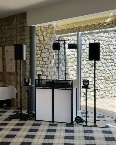 Eine DJ-Kabine mit Lautsprechern, Licht und Ausrüstung ist drinnen in der Nähe einer Steinmauer und großer Fenster mit einem karierten Teppichboden aufgebaut - perfekt für diejenigen, die Firmen Weihnachtsfeier Österreich auflegen wollen. Das Sonnenlicht strömt durch das Fenster herein und erhellt den Raum.